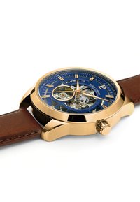 Gold-tone watch with a blue skeleton dial, brown leather strap, and prominent crown. Features silver hour markers and intricate mechanics.