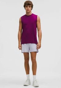 Ärmlös lila träningsskjorta i kombination med ljuslila shorts. Modell som bär vita träningsskor och vita strumpor. Enkelt mönster, figurnära passform.
