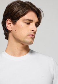 Biała koszulka z krótkim rękawem i okrągłym dekoltem. Gładka tekstura i dopasowany krój. Dyskretny haftowany logo na piersi.