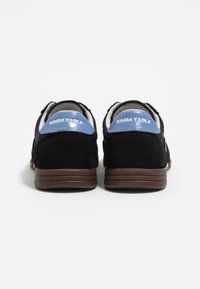 Schwarze Wildledersneaker mit blauen Lacklederakzenten, ausgestattet mit einer runden Spitze, einem gepolsterten Schaft und einer braunen Gummisohle. Die Markenkennzeichnung ist an der Ferse angebracht.