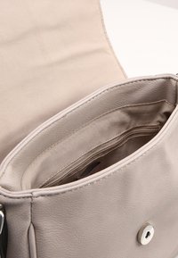 Světle šedý kožený interiér kabelky s měkkou textilní podšívkou. Obsahuje hlavní přihrádku a kapsu na zip pro snadnou organizaci.