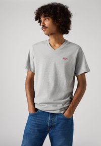 Siva V-izrez majica od bombaža, ima kratke rukave, crven Levi's logo na lijevoj strani prsnog područja, uparena s plavim trapericama.