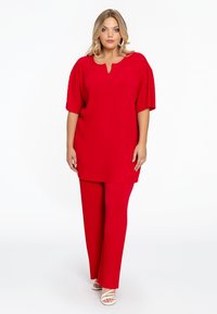 Rode geribbelde tweedelige outfit met een losvallend shirt met korte mouwen en een V-hals, gecombineerd met rechte broekspijpen.