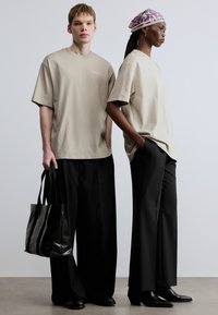 Tricouri supradimensionate bej, pantaloni negri largi, pantofi negri din piele și o eșarfă mov cu model. Geantă tote neagră ținută de o persoană.