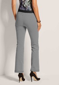 Zwart-wit zigzagpatroon broek met een flared ontwerp en een elastische tailleband, gecombineerd met zwarte hoge hakken.