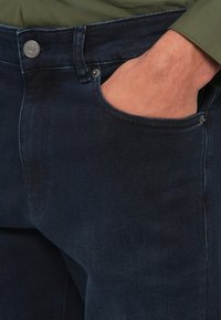 Tumši zili džinsa džinsi ar klasisku piecu kabatu dizainu, sudraba pogu un viegli izbalējušu auduma tekstūru.