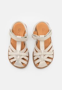 Sandalias de cuero beige con un diseño de tiras entrecruzadas, correa de tobillo ajustable y plantilla texturizada. Suela plana con detalles cosidos.