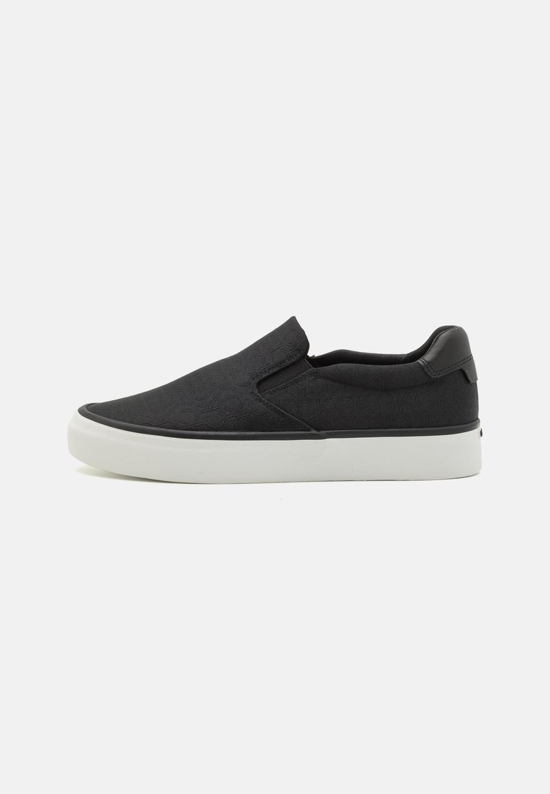 Svarte slip-on sko med en teksturert overdel som har et subtilt mønster, komplementert av en hvit gummisåle og en svart hælakse.