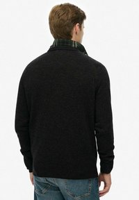Zwarte wollen trui met een hoge kraag, met daaronder een groen ruitpatroon. Het ontwerp is figuurknap, met lange mouwen en een gladde textuur.
