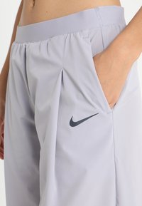 Bermudas deportivas de color gris claro con una textura suave, cinturilla elástica, pliegues en la parte delantera y un logo de Nike en gris oscuro en el bolsillo lateral.