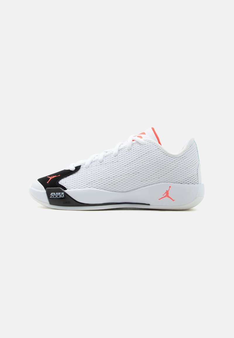 Λευκό και μαύρο χαμηλό sneaker με επάνω μέρος από δίχτυ, πορτοκαλί λογότυπα Jumpman, λευκά κορδόνια και ετικέτα "Air Zoom" στη σόλα κοντά στα δάχτυλα.
