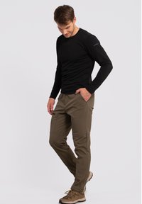 Sort langærmet skjorte parret med olivengrønne softshellbukser med lommer og en glat, strækbar tekstur. Beige vandrestøvler fuldender outfittet.