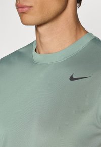 Lys grøn sportstrøje med en glat tekstur og rund halsudskæring. Har et lille sort Nike swoosh-logo på brystet.