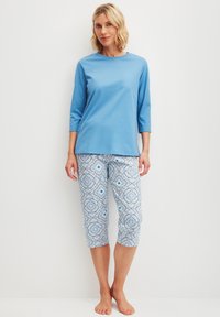 Blaues Baumwolloberteil mit drei Viertelärmeln, kombiniert mit gemusterten Capris, die geometrische Designs in Blau und Weiß aufweisen. Lässiges, leichtes Outfit.