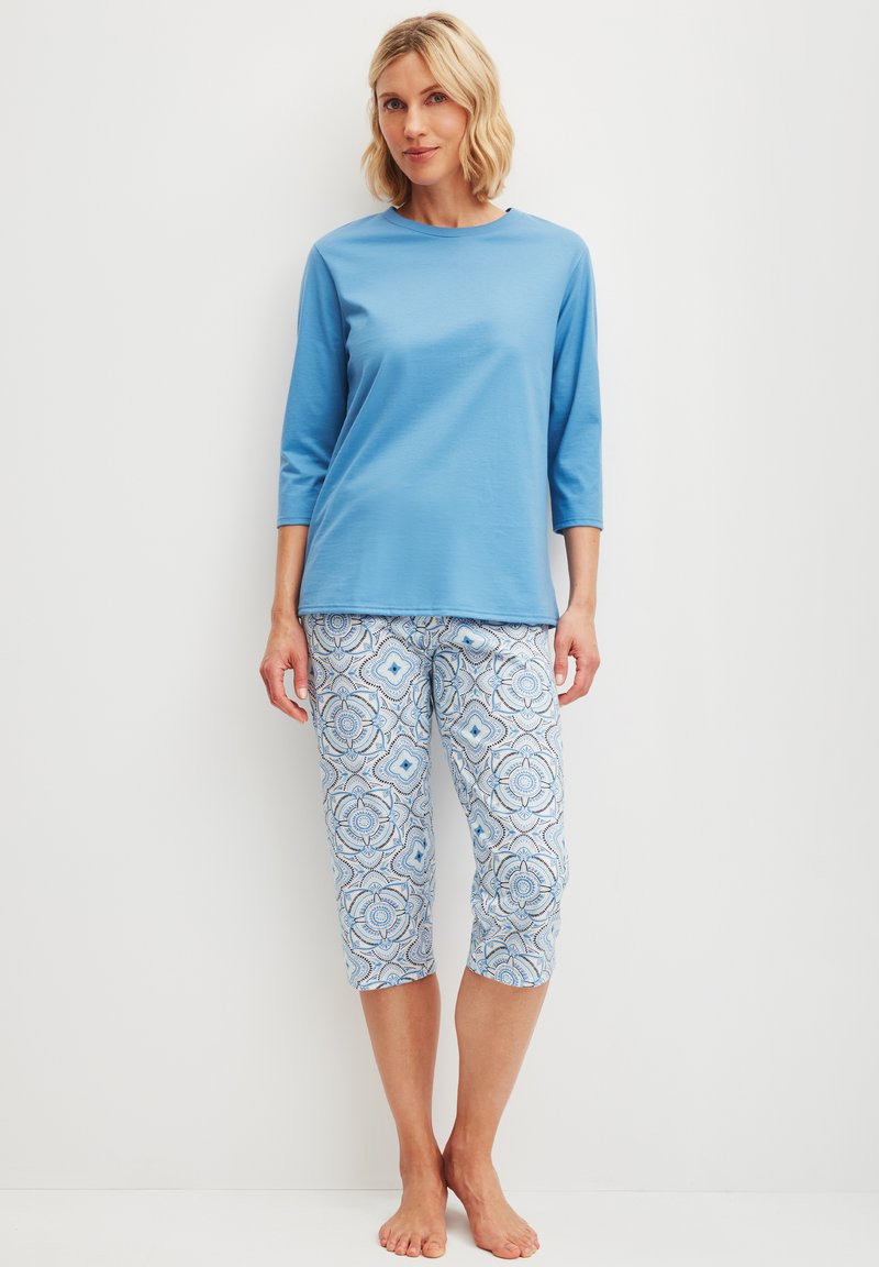 Blaues Baumwolloberteil mit drei Viertelärmeln, kombiniert mit gemusterten Capris, die geometrische Designs in Blau und Weiß aufweisen. Lässiges, leichtes Outfit.