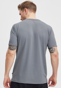 Šedé sportovní tričko s krátkým rukávem vyrobené z texturované tkaniny, s kulatým výstřihem a plochými švy. Na rukávu je decentní logo.