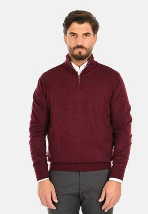 Maglione bordeaux con collo zip, polsini a coste e una texture liscia, abbinato a una camicia bianca con colletto underneath.