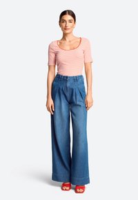 Striped red and white fitted top with short sleeves, paired with wide-leg blue denim trousers. Model wearing red platform sandals.