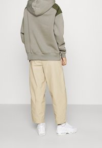 Sudadera gris con capucha y detalles verdes, de corte oversize. Combinada con pantalones holgados beige claros y zapatillas blancas. Textura de tela suave.