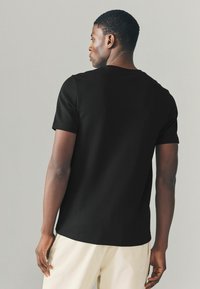 Sort kortærmet t-shirt i bomuld, med rund hals og en afslappet pasform. Baglæns visning fremhæver den glatte tekstur og subtile syninger.