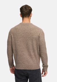 Brun strikket sweater med runde hals, ribbede ærmer og kant, struktureret stof, båret over mørke jeans, set fra bagsiden.