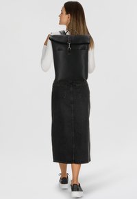 Sac à dos noir à rabat en matériau lisse, avec une fermeture à clip, un design minimaliste, et deux bretelles.