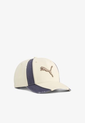 Beige og marineblå baseballcap med buet skygge, som har et brunt Puma-logo foran og små slidte detaljer på siderne og skyggen.