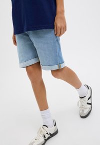 Pantaloni di jeans azzurri chiari con risvolti, dalla vestibilità dritta, indossati con calze bianche e scarpe sportive con accenti neri e grigi.