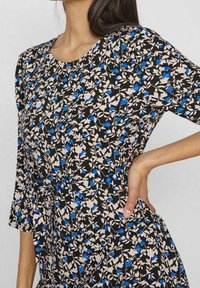 Robe à imprimé floral avec un fond noir et des motifs floraux bleus et beiges, col rond et manches courtes. Texture de tissu douce.