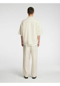 Lys beige oversized skjorte med slagkrage, korte ermer og matchende lyse bukser. Antrekket er laget av mykt, teksturert stoff.