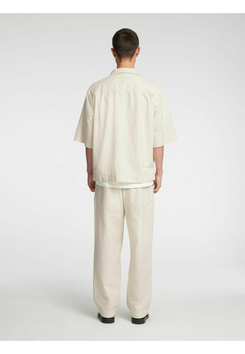 Lys beige oversized skjorte med slagkrage, korte ermer og matchende lyse bukser. Antrekket er laget av mykt, teksturert stoff.