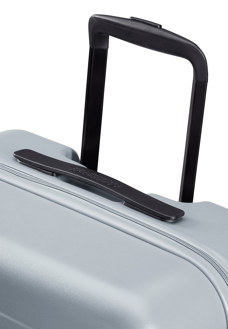 Mango telescópico y asa de transporte en una maleta rígida de color gris claro con cierre de cremallera.