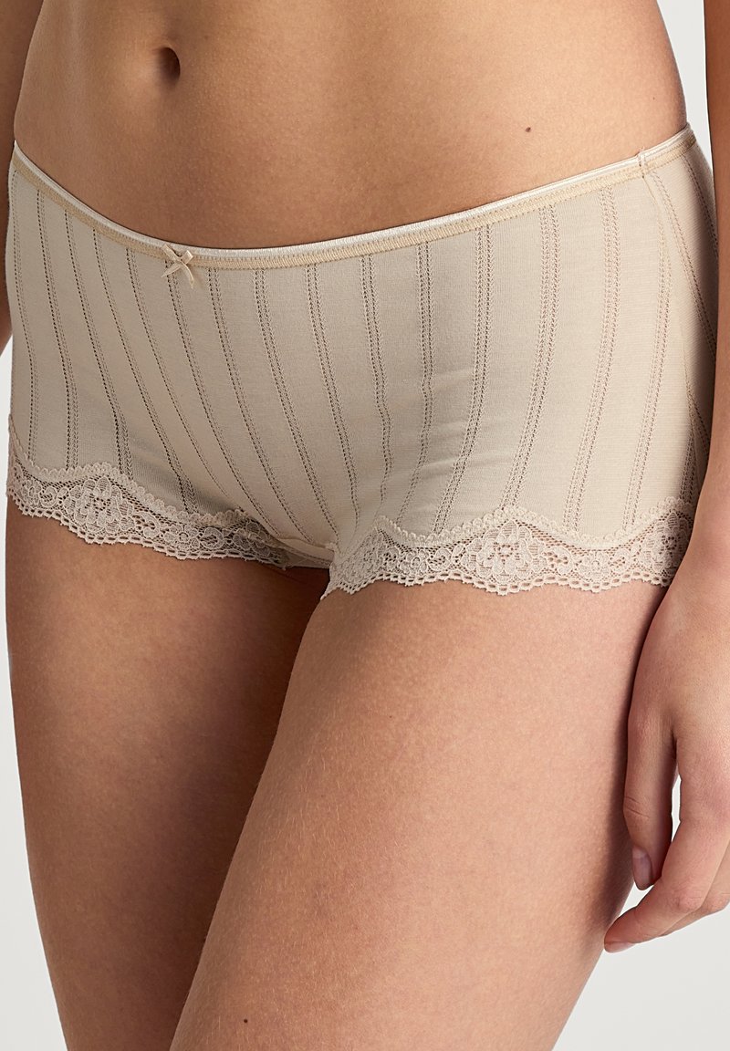 Pantaloni corti beige in cotone misto con strisce verticali, rifinitura in pizzo alle aperture delle gambe e un piccolo fiocco in vita. Texture morbida.