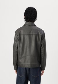 Men's dark gray leather jacket with a smooth texture, notched collar, and visible stitching details. Paired with dark denim trousers.