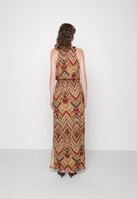 Maxikleid mit Chevron-Muster in warmen Tönen von Gold, Rot und Braun, mit taillierter Taille und ärmellosem Design. Glatte Stofftextur.