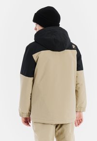 Beige und schwarze Kapuzenjacke mit elastischen Bündchen, wasserabweisendem Material und Logodetail auf der Rückseite. Glatte Textur, reguläre Passform, entworfen für Wärme.