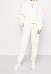 White fleece hoodie with logo, paired with matching sweatpants. Features drawstring waist and cuffs. White sneakers with pink accents.