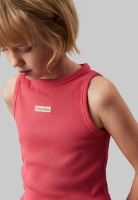 Top sin mangas de ajuste slim, de canalé en color coral, con un cuello redondo y una pequeña etiqueta con el logo de Calvin Klein en el pecho. Textura suave.
