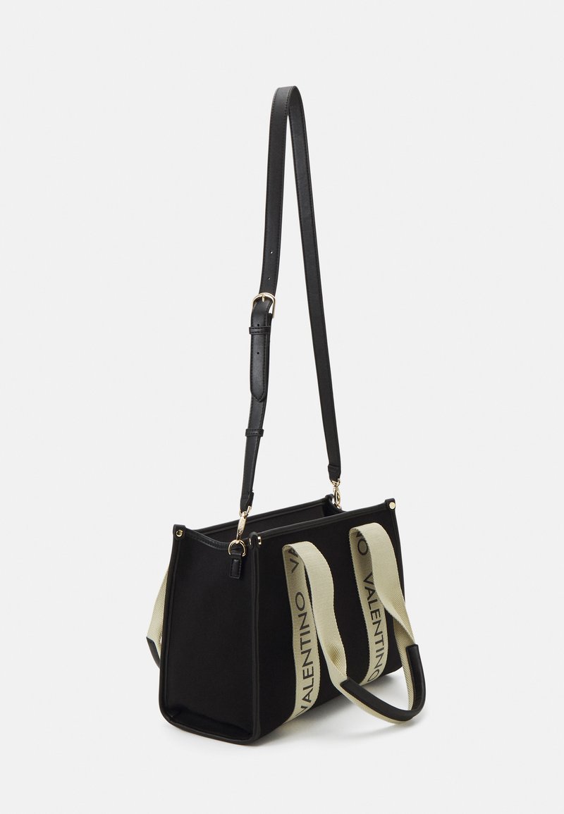 Bolsa tote negra con correa de cuero ajustable y asas de lienzo beige que presenta el texto "VALENTINO". Forma estructurada con acentos de hardware dorado.