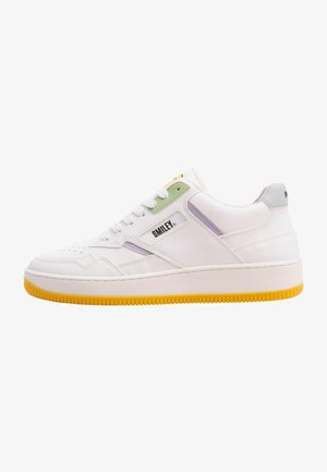 Zapatilla blanca con cuero texturizado, suela de goma amarilla, acentos en verde y morado, y un logo en el lateral. Punta redondeada y diseño con cordones.