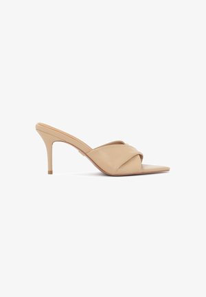 Mules beiges à talons hauts avec un bout pointu, en cuir lisse et au design de brides croisées. Le talon aiguille fin renforce l'élégance.