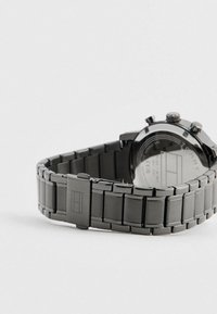 Orologio da polso in acciaio inox nero con bracciale a maglie e chiusura, che mostra il logo del marchio inciso sulla chiusura e dettagli incisi sul retro dell'orologio.