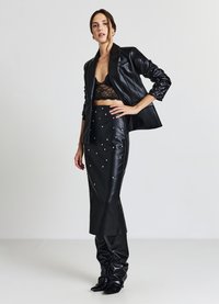 Completo in pelle nera composto da un reggiseno corto in pizzo, un blazer su misura con maniche testurizzate e una gonna lunga impreziosita da borchie argento.