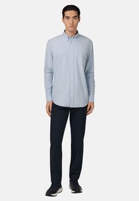 Chemise bleu clair à boutons avec une poche poitrine, manches longues et ourlet arrondi, associée à un pantalon marine et des baskets sombres.