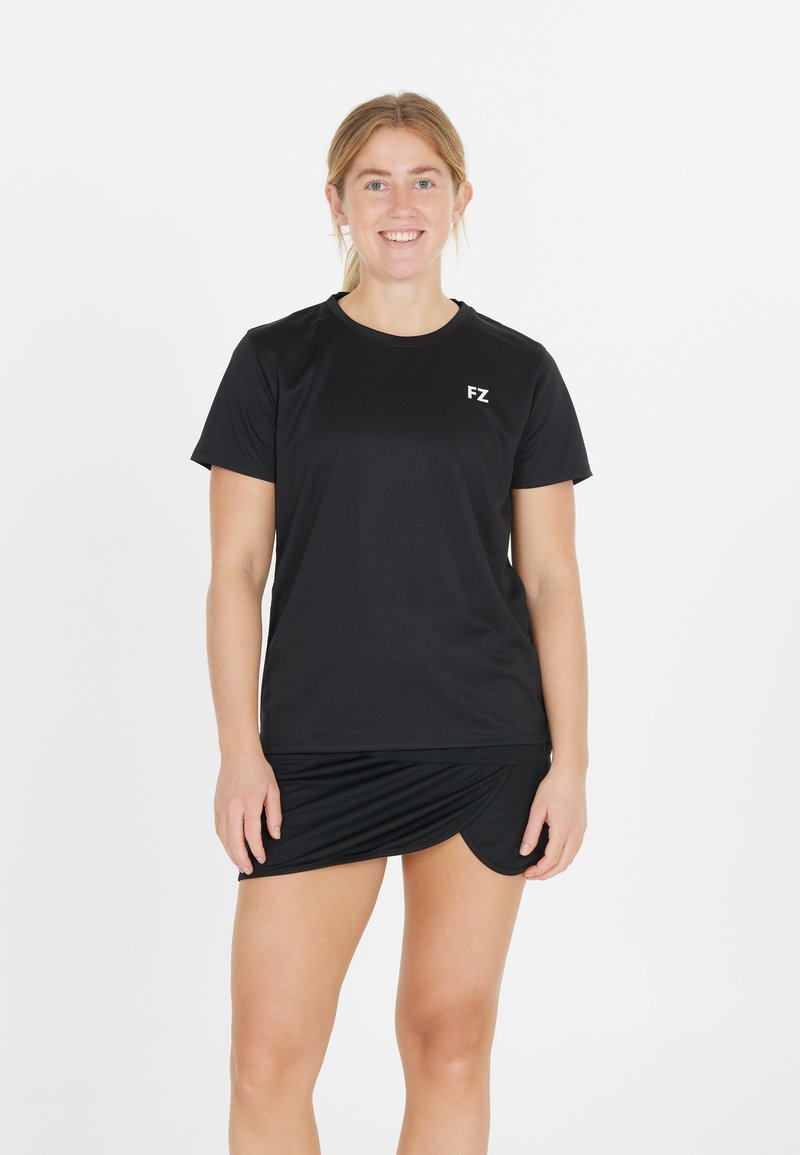 Nuori nainen hymyilee seisten, päällään musta lyhythihainen urheilupaita, jossa on "FZ"-logo, sekä mustat urheiluhameet valkoista taustaa vasten.