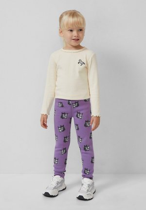 Lange mouwen crèmekleurig geribbeld top met een paardenborduursel; paarse leggings met zwarte hondenprints; witte sneakers met grijze accenten; klokmouwen.