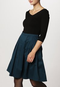 Top negro de manga larga combinado con una falda plisada color teal, hecha de un material suave, con un cuerpo ajustado y un dobladillo acampanado.