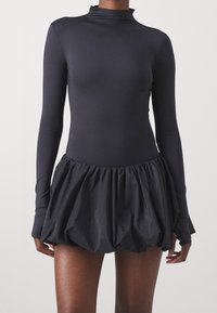 Body noir à manches longues avec un col montant, associé à une jupe noire volumineuse et froncée en tissu texturé.