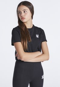Černé bavlněné tričko s krátkým rukávem, s bílým logem na levé hrudi. V kombinaci s černými legíny, elegantní design, přiléhavý střih.