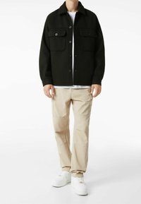 Černá sako na knoflíky se dvěma náprsními kapsami, nošeno přes bílé tričko, v kombinaci s béžovými cargo kalhotami a bílými teniskami.